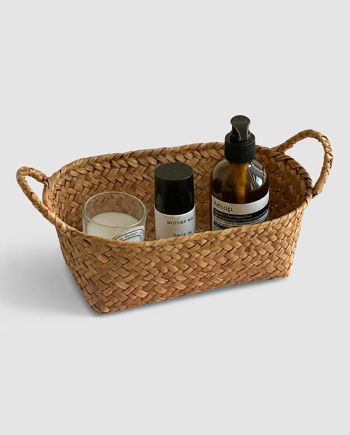 Birgit grass woven cosmetic storage basket with loop handles holding bath and beauty products