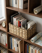 Inga grass woven storage basket holding books and stationery on a wooden bookshelf