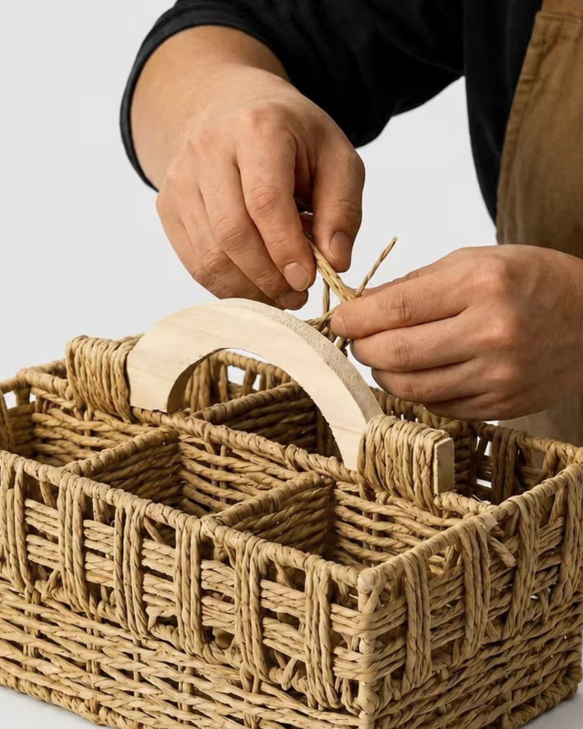 Artisan weaving paper rope around the arched wooden handle of the Lina remote caddy