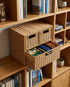 Mikkel faux rattan drawer storage cabinet holding folded clothing and accessories on a bookcase shelf