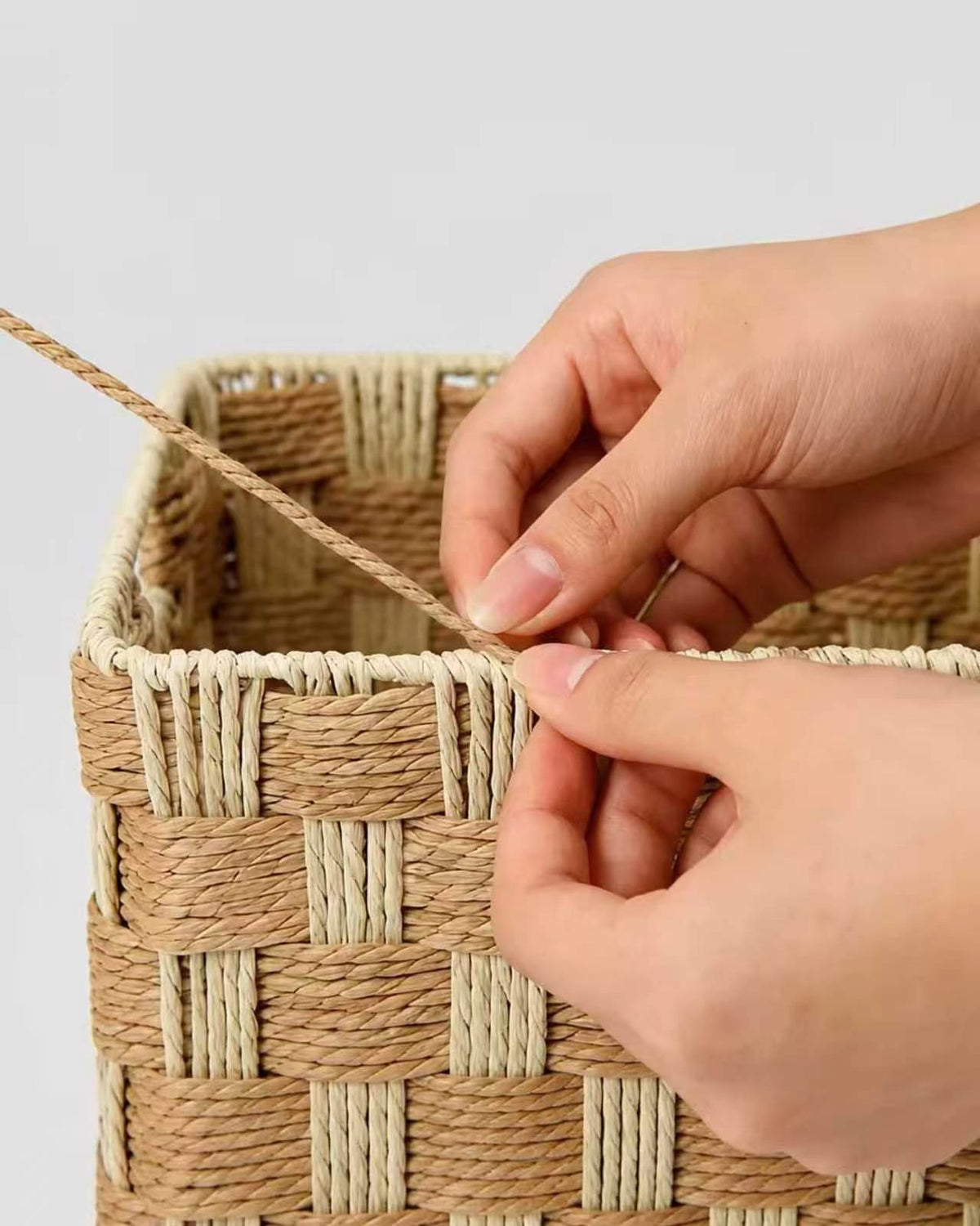 Artisan handweaving the natural two-tone paper rope pattern of a Siv makeup basket