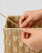 Artisan handweaving the natural two-tone paper rope pattern of a Siv makeup basket